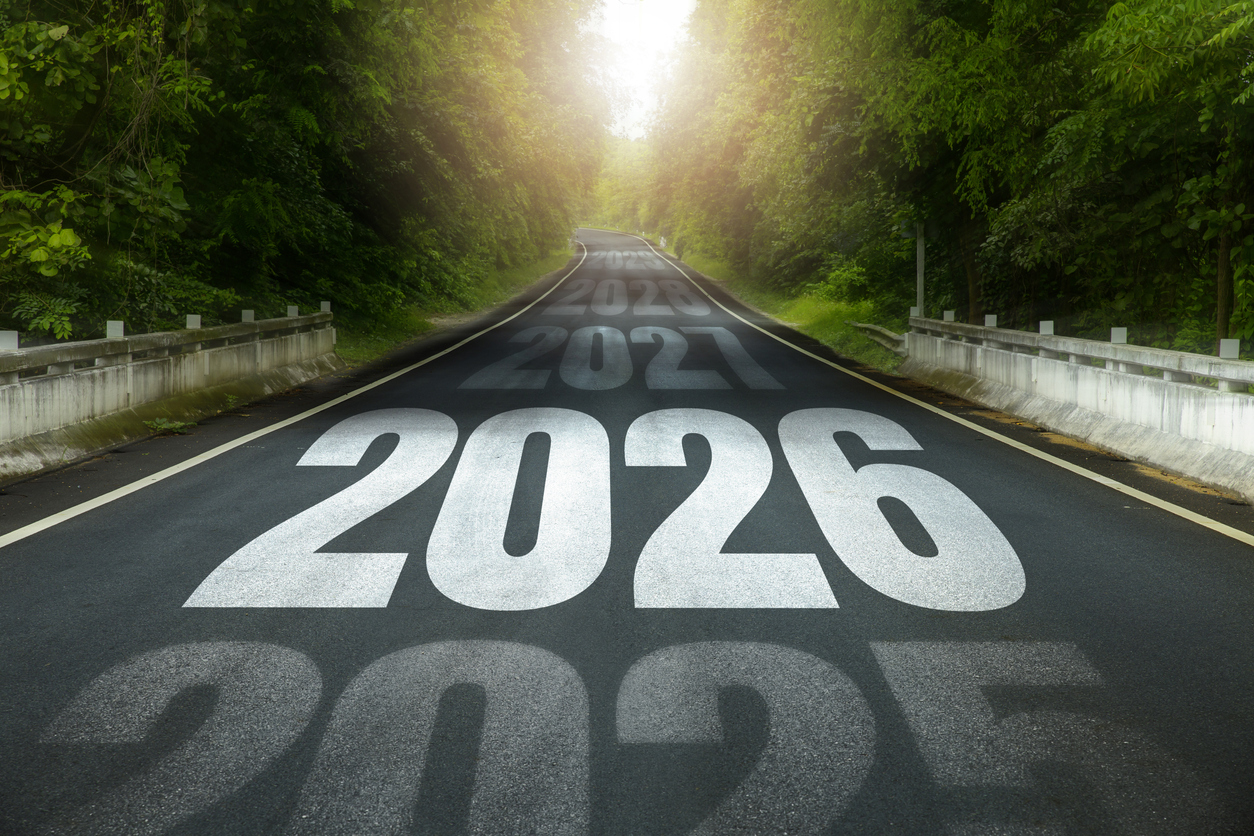Long road through green forest with large 2026 painted on asphalt and earlier years fading ahead, symbolizing the path to goals, roadmap, planning, progress, motivation, growth and success new year. Asphalt road through a green forest with “2026” painted on the pavement, representing emerging asphalt industry trends and the future of sustainable road construction.