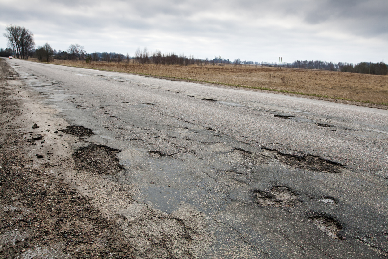 Damaged road Worn and damaged roadway with visible cracks and potholes, demonstrating how extreme temperatures and moisture can degrade pavement over time.