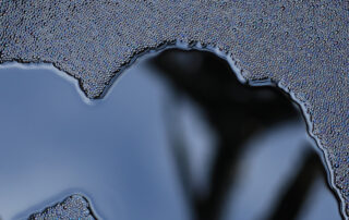 Abstract close-up of black liquid bitumen surface with glossy, flowing texture, representing asphalt emulsions before breaking and curing in pavement applications.