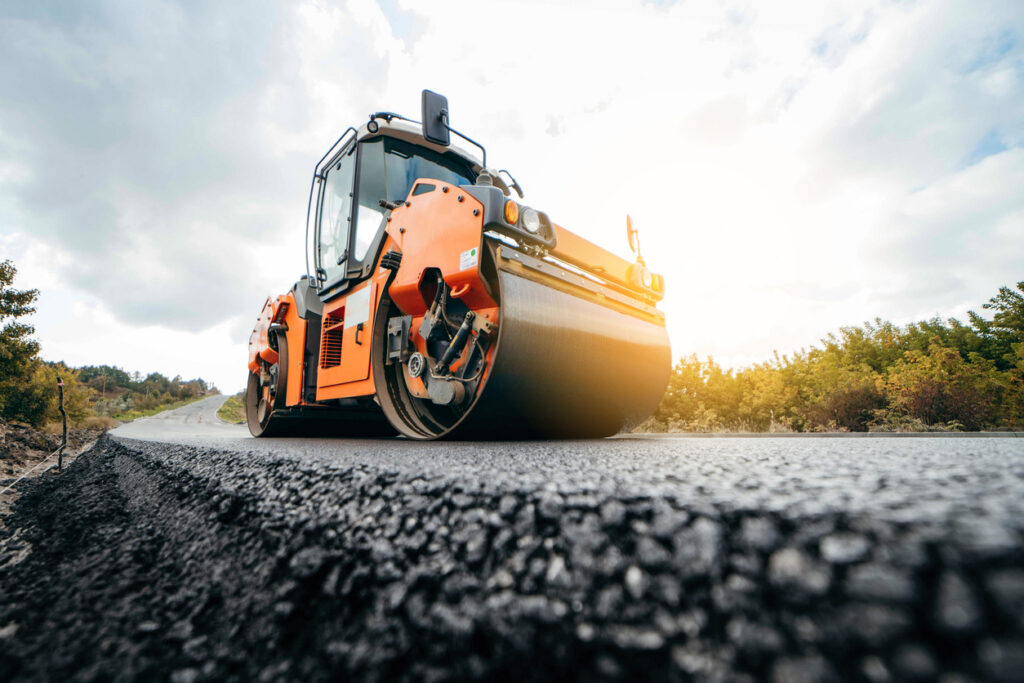 Vibratory asphalt roller compactor compacting new asphalt pavement. Road service repairs the highway Vibratory asphalt roller compacting fresh road surface, illustrating the role of asphalt performance enhancers in pavement construction and durability improvement.