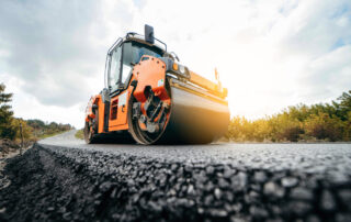 Vibratory asphalt roller compacting fresh road surface, illustrating the role of asphalt performance enhancers in pavement construction and durability improvement.