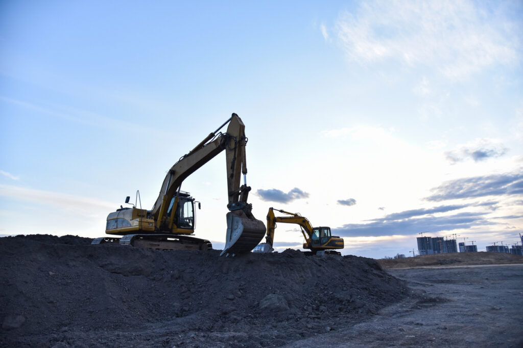 Excavators work at constrruction site on sunset background. Backhoe digs gravel and old concrete Two excavators at a highway construction site loading old, torn-up road debris at sunset, representing the processing of reclaimed asphalt pavement before applying different types of bitumen additives.