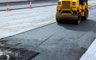 Heavy roller compacting newly paved asphalt roadway, representing warm mix asphalt technology, reduced fuel consumption, and asphalt plant efficiency.