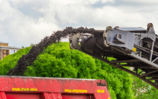 A cold milling machine removing aged asphalt pavement and conveying milled asphalt (RAP) into a dump truck for recycling.