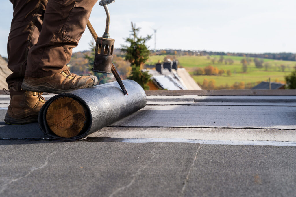 Worker Heating and melting bitumen roofing Flat roof installation. Worker heating bitumen for flat roof installation, illustrating bitumen-based roofing compounds and the importance of process-friendly roofing formulations.