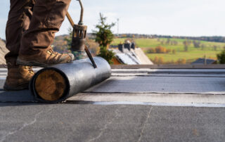 Worker heating bitumen for flat roof installation, illustrating bitumen-based roofing compounds and the importance of process-friendly roofing formulations.