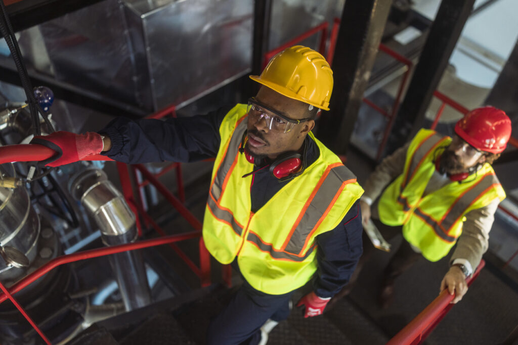 Multiethnic Technicians Ascending Plant Stairs Technicians inspecting industrial equipment at an asphalt production facility using advanced crosslinking agents for PMB to improve efficiency and reduce equipment fouling.