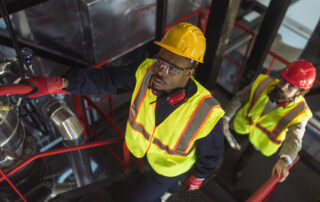 Technicians inspecting industrial equipment at an asphalt production facility using advanced crosslinking agents for PMB to improve efficiency and reduce equipment fouling.
