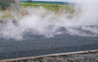 Steaming hot asphalt mat laid during roadwork, illustrating the high heat exposure and fumes produced by conventional hot mix paving.